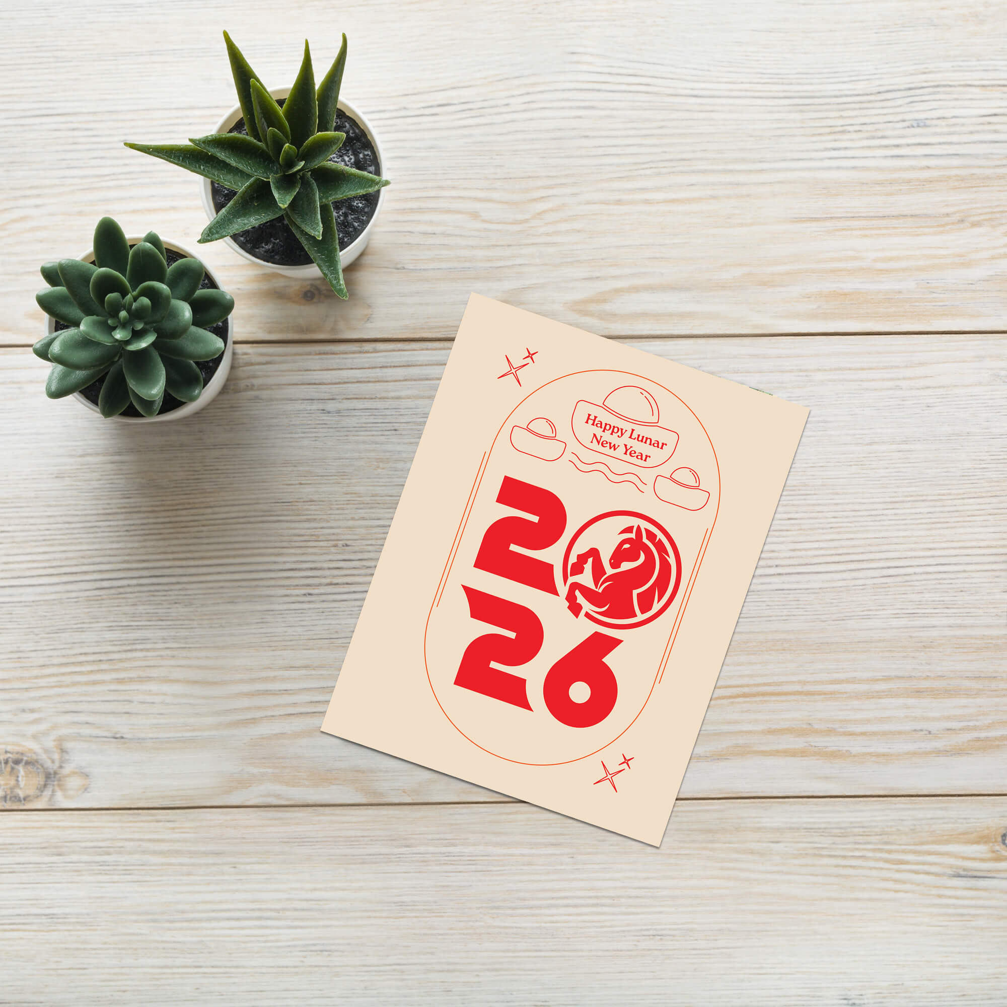 Card with red text and dragon design on a wooden surface with succulents