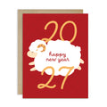 A chinese new year card with a kraft envelope behind it, featuring a white cartoon sheep and gold and red text reading '2027 happy new year'.
