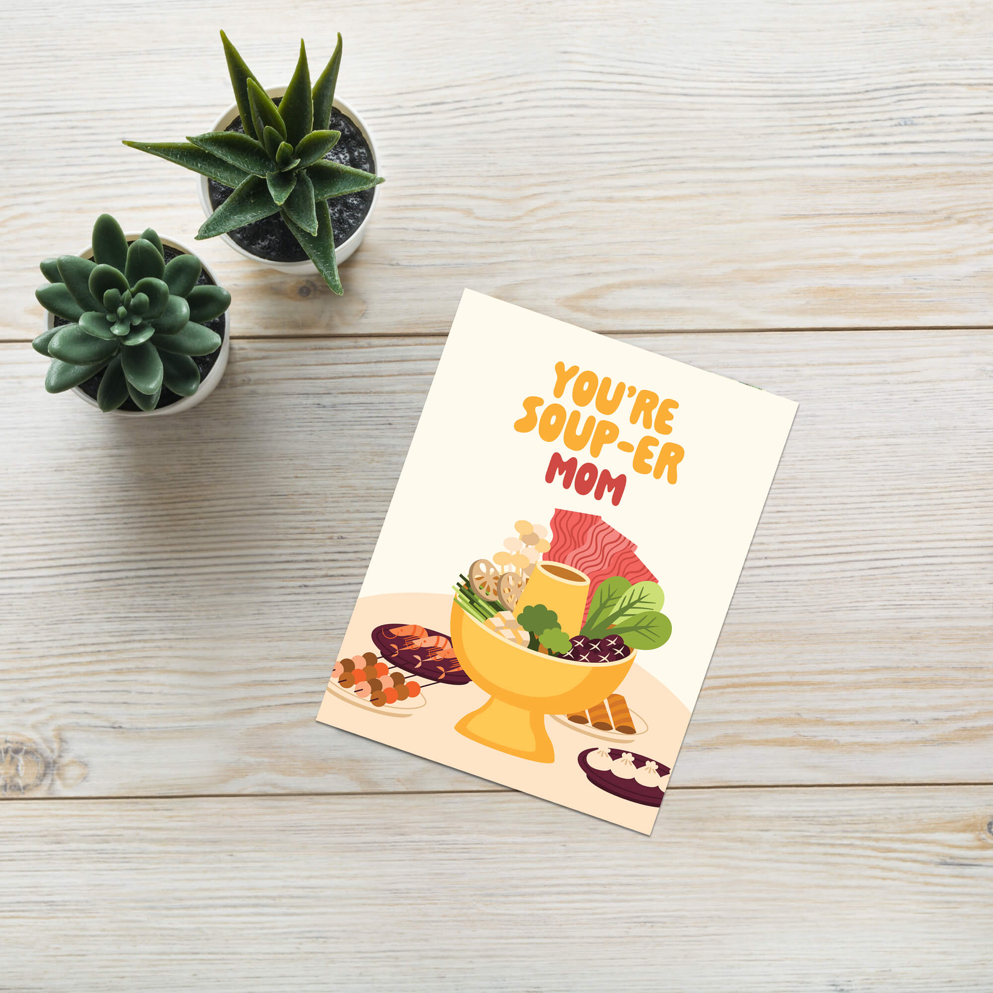 asian Greeting card with 'You're Soup-er Mom' text on a wooden surface with plants.
