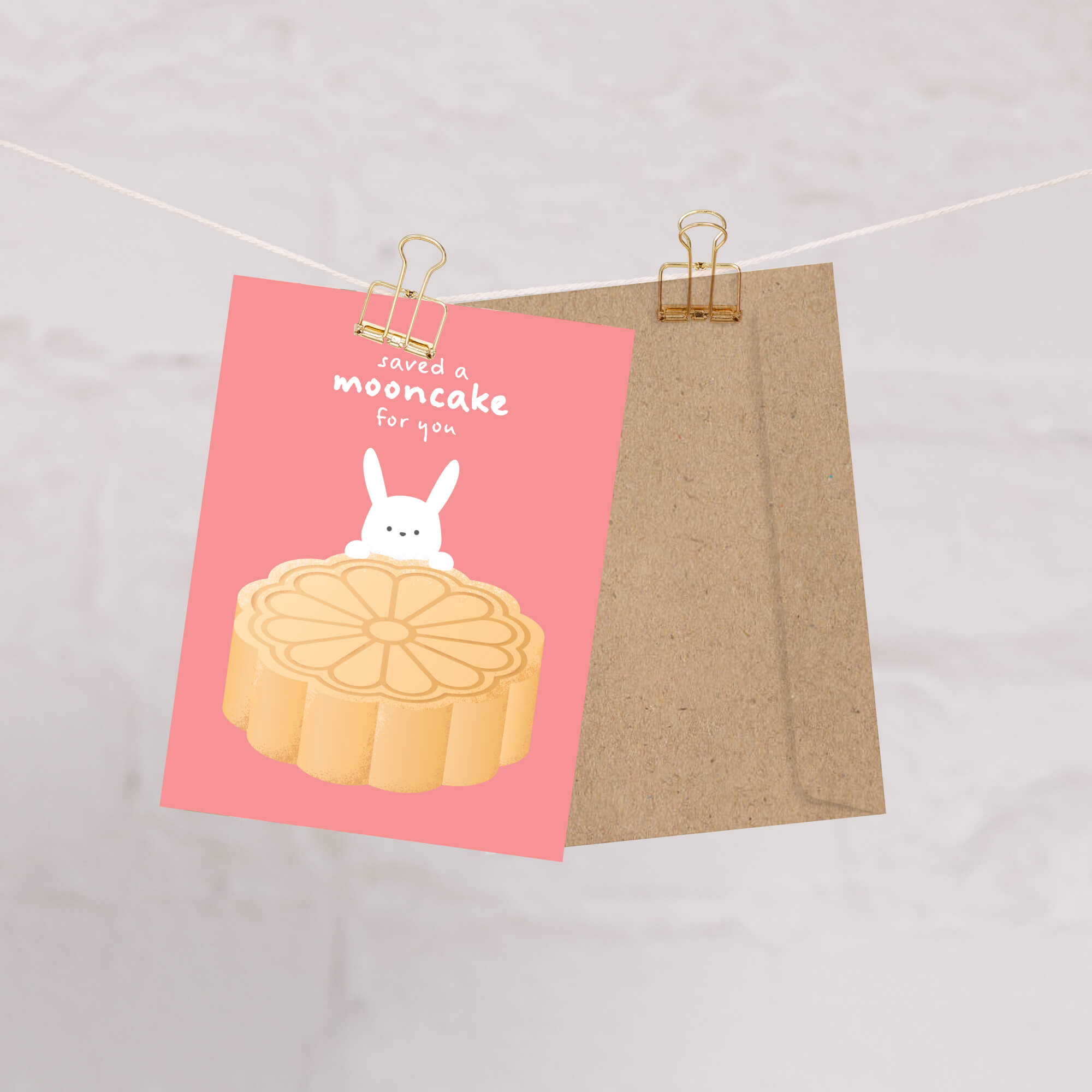 Card with a mooncake illustration and text on pink paper, clipped to a string.