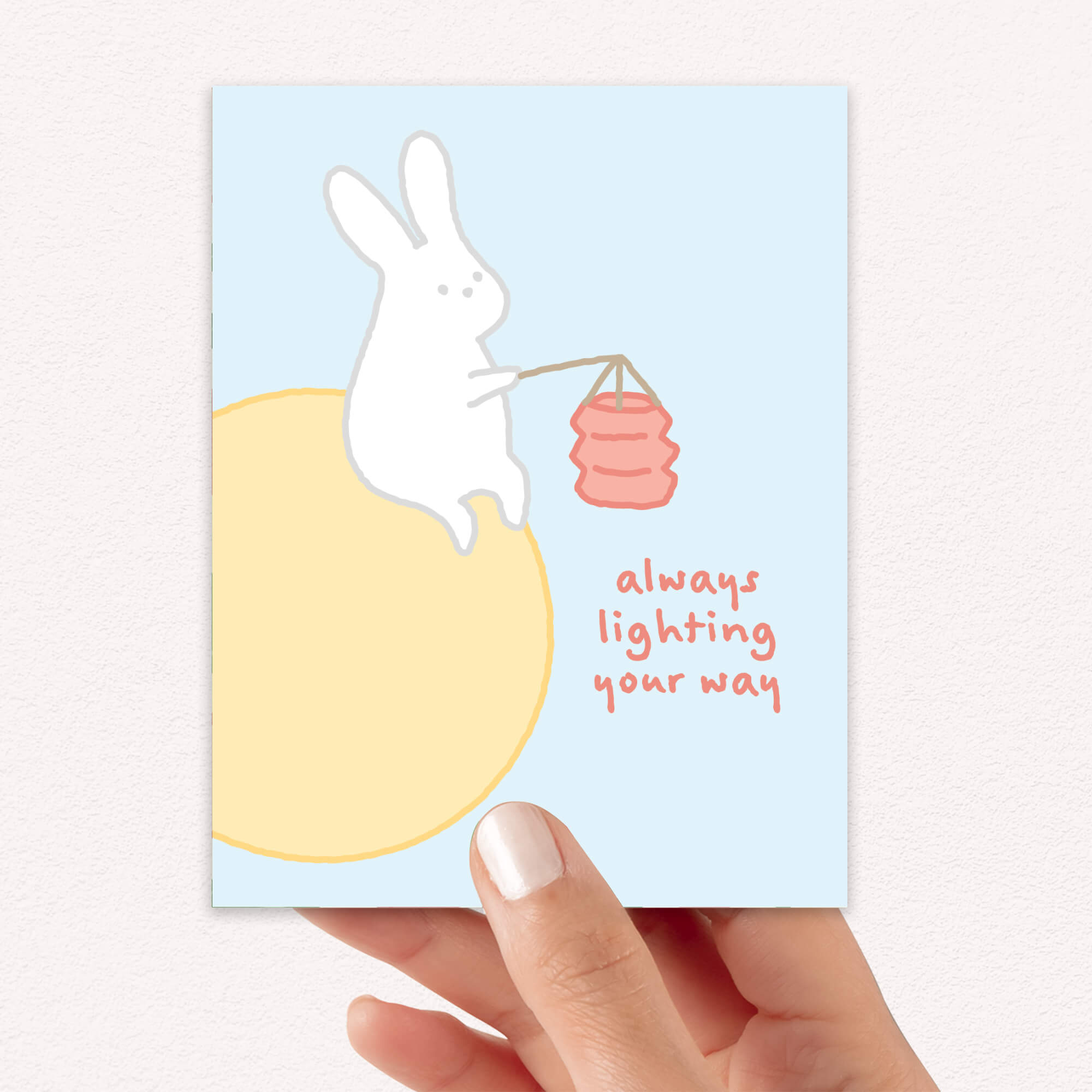 asian inspired Greeting card with a rabbit holding a lantern and text 'always lighting your way' on a light blue background. for mid autumn festival