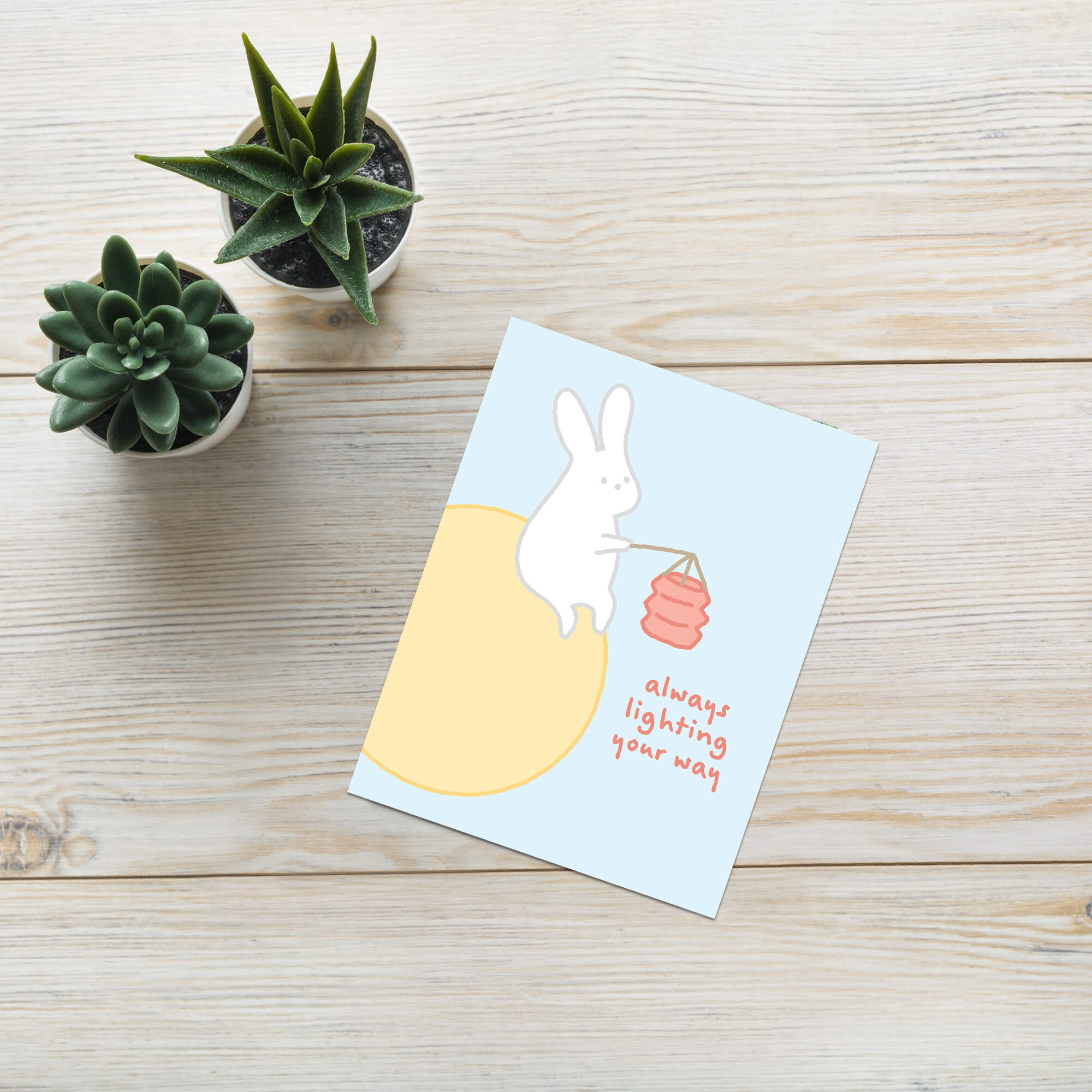 asian inspired Greeting card with a rabbit holding a lantern and text 'always lighting your way' on a light blue background. for mid autumn festival