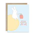 asian inspired Greeting card with a rabbit holding a lantern and text 'always lighting your way' on a light blue background. for mid autumn festival