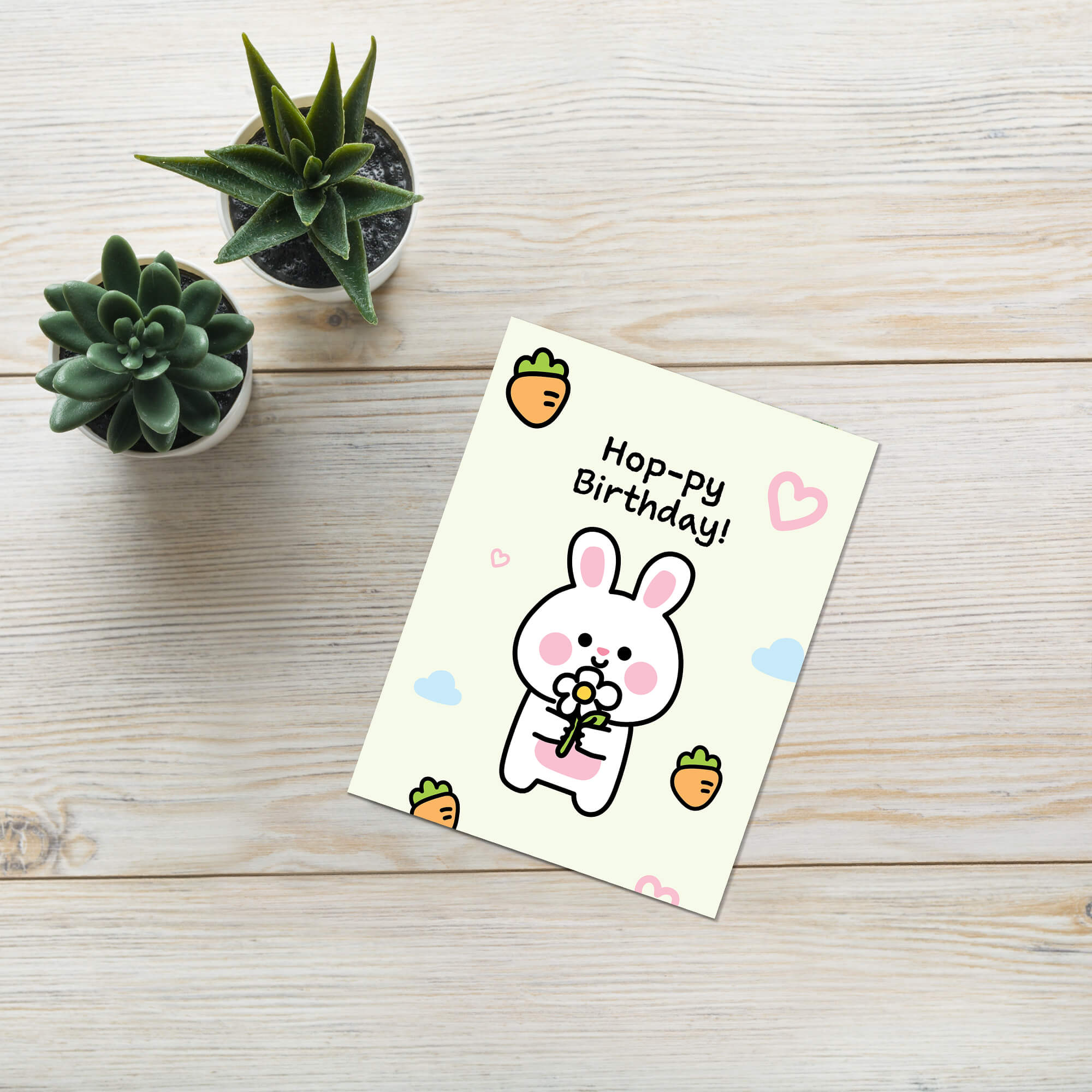 Birthday card with a cartoon rabbit and 'Hoppy Birthday!' text on a wooden surface with small plants.