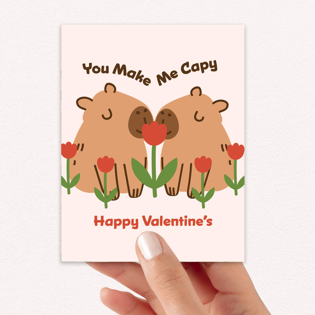 Two capybaras with tulips; curved text “You Make Me Capy” and “Happy Valentine’s.”