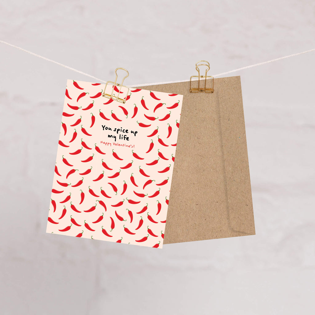 light pink valentines day card with repeating red chilies and center text “You spice up my life — Happy Valentine’s.”