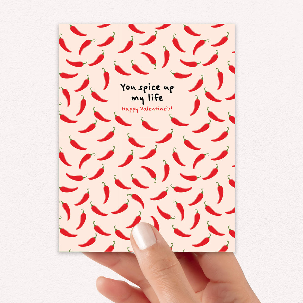 light pink valentines day card with repeating red chilies and center text “You spice up my life — Happy Valentine’s.”