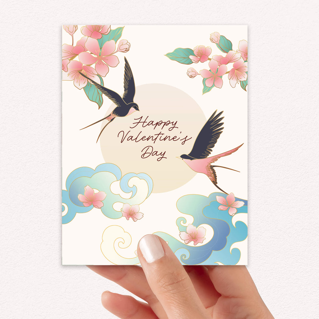 Two swallows flying near blossoms and pale sun with “Happy Valentine’s Day.”