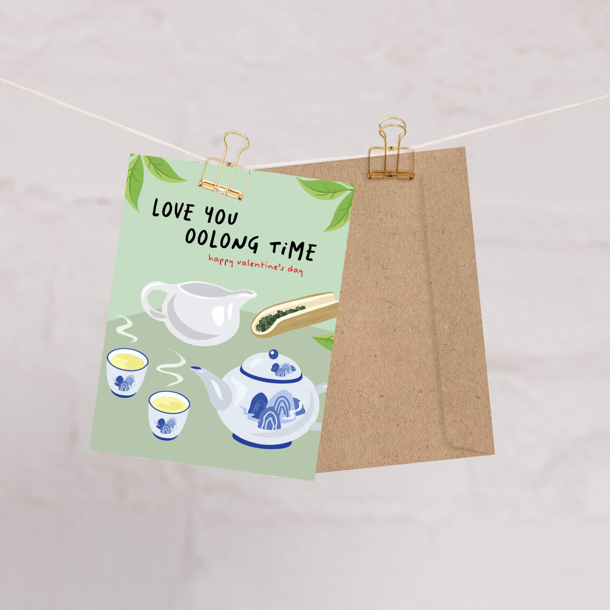 asian inspired valentintues day card with White and blue china teapot, cups, and oolong loose leaf tea on soft green; text “Love you oolong time.”