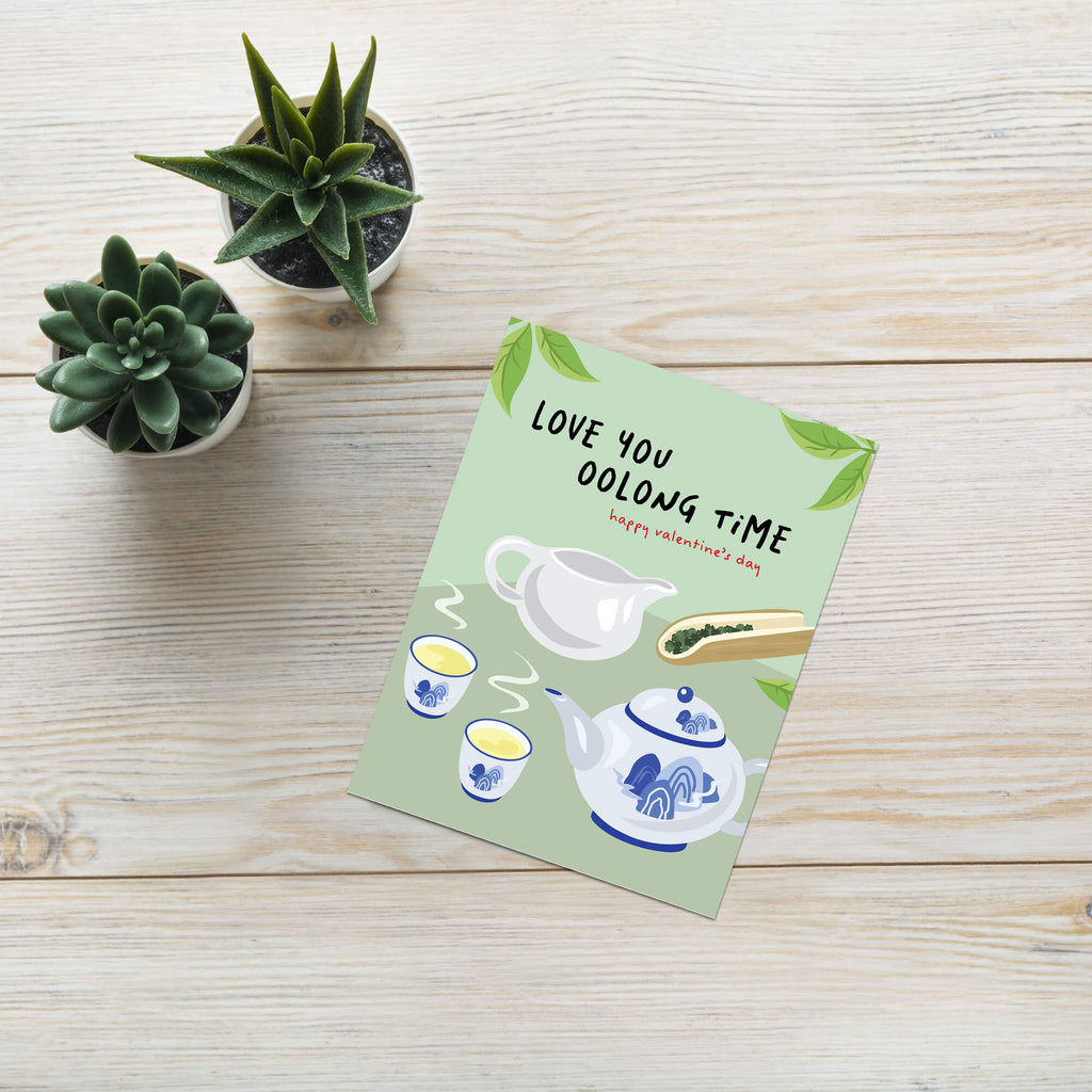 asian inspired valentintues day card with White and blue china teapot, cups, and oolong loose leaf tea on soft green; text “Love you oolong time.”