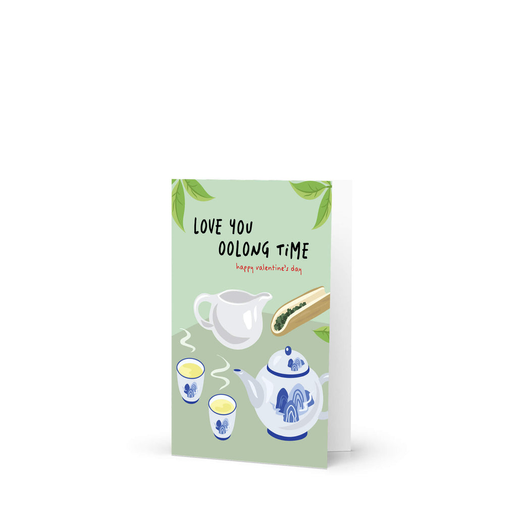 asian inspired valentintues day card with White and blue china teapot, cups, and oolong loose leaf tea on soft green; text “Love you oolong time.”