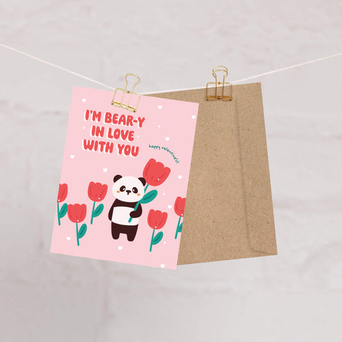 Panda holding tulip among pink flowers; text “I’m bear-y in love with you — happy valentine’s!”
