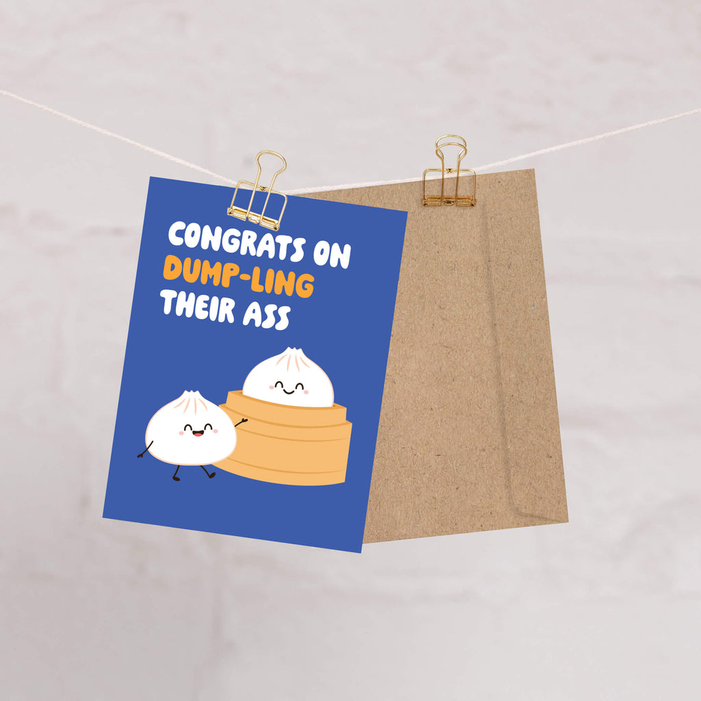 Card with cartoon dumplings and humorous text on a blue background, clipped to a string.