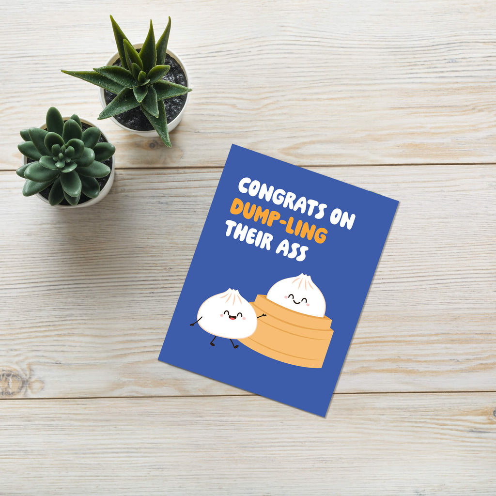 Greeting card with cartoon dumplings and humorous text on a wooden surface with plants.