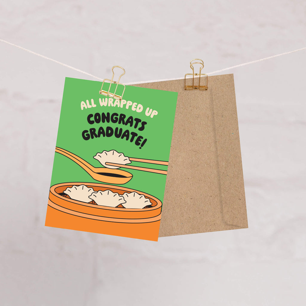 Graduation card with dumplings and text 'All Wrapped Up Congrats Graduate!' on a green background.