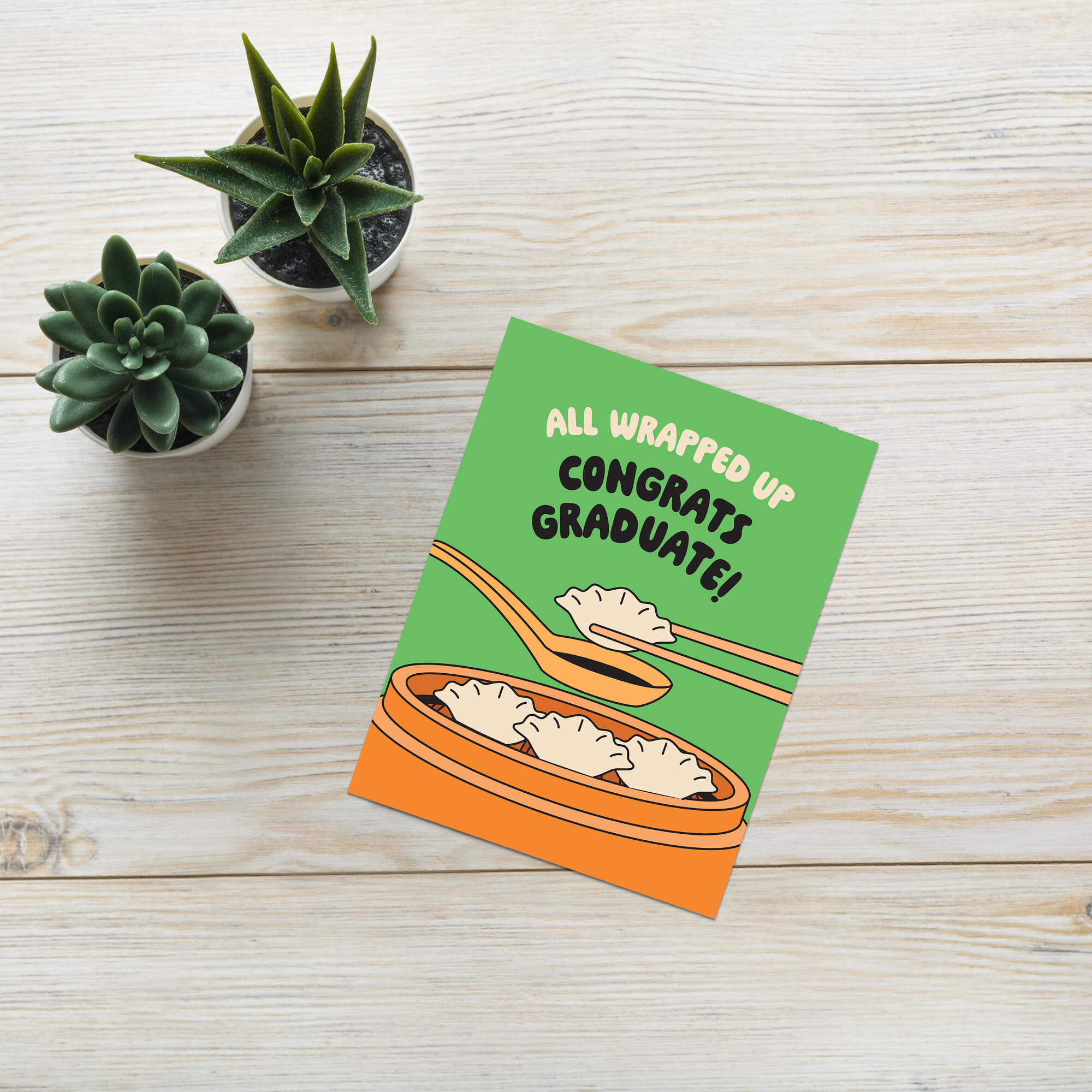 Graduation card with dumplings and text 'All Wrapped Up Congrats Graduate!' on a green background.
