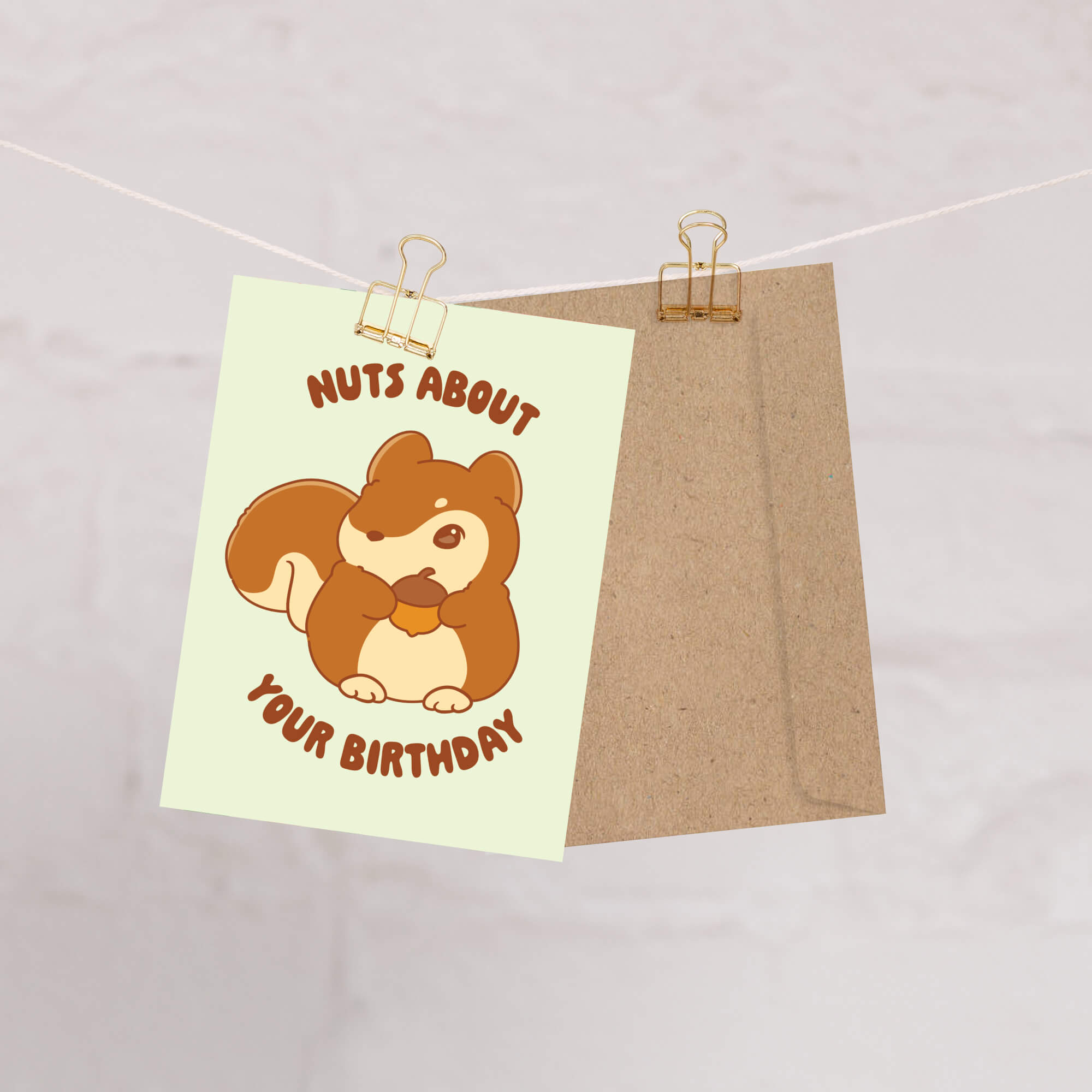 Cartoon squirrel holding a nut with text 'Nuts About Your Birthday' on a light green card, attached to a brown paper bag with a clothespin.
