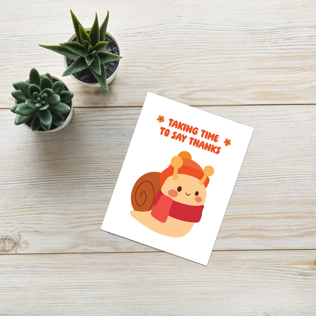 autumn Greeting card with a snail illustration and text 'Taking time to say thanks' on a wooden surface with small plants.