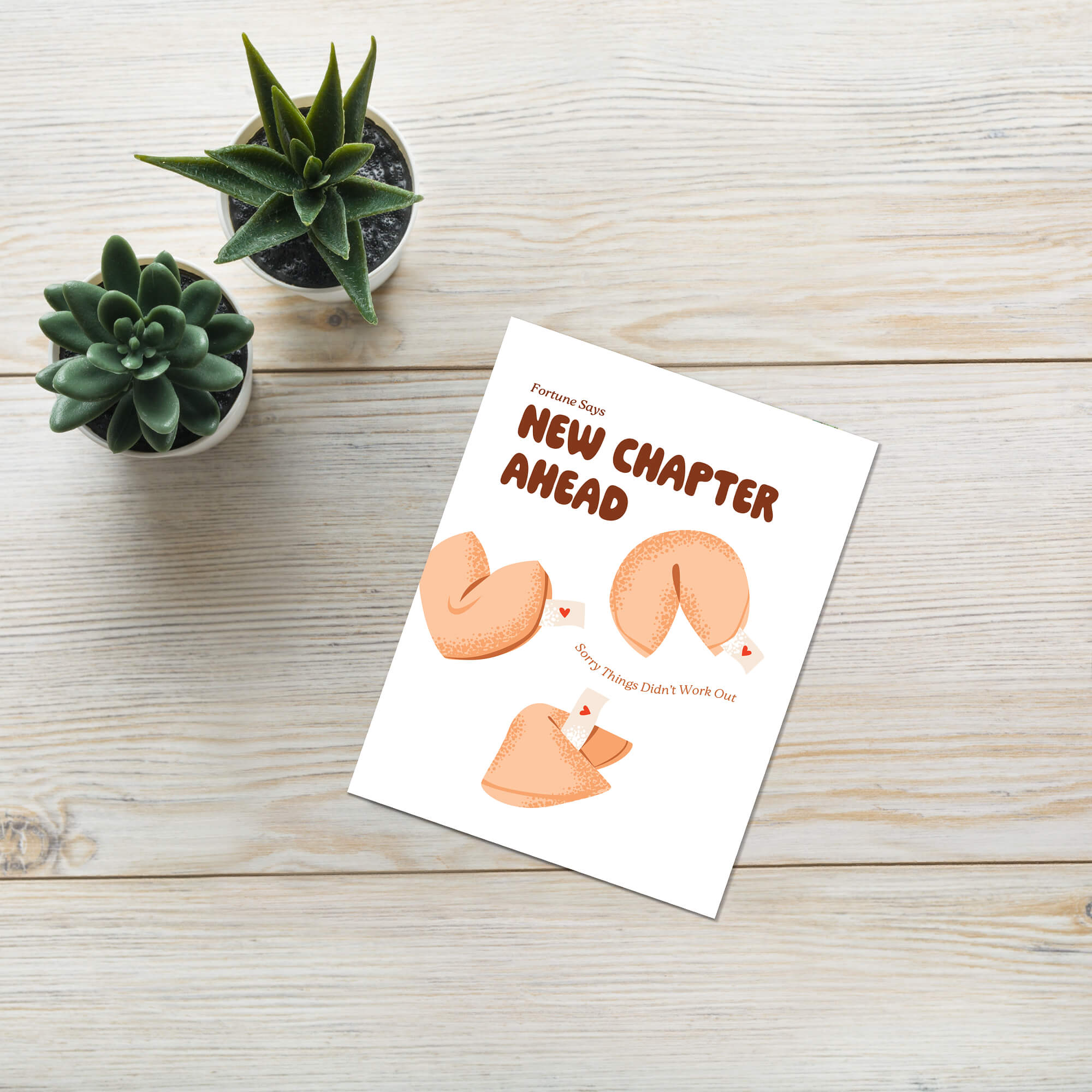 Greeting card with fortune cookies and 'New Chapter Ahead' text on a wooden surface with plants.