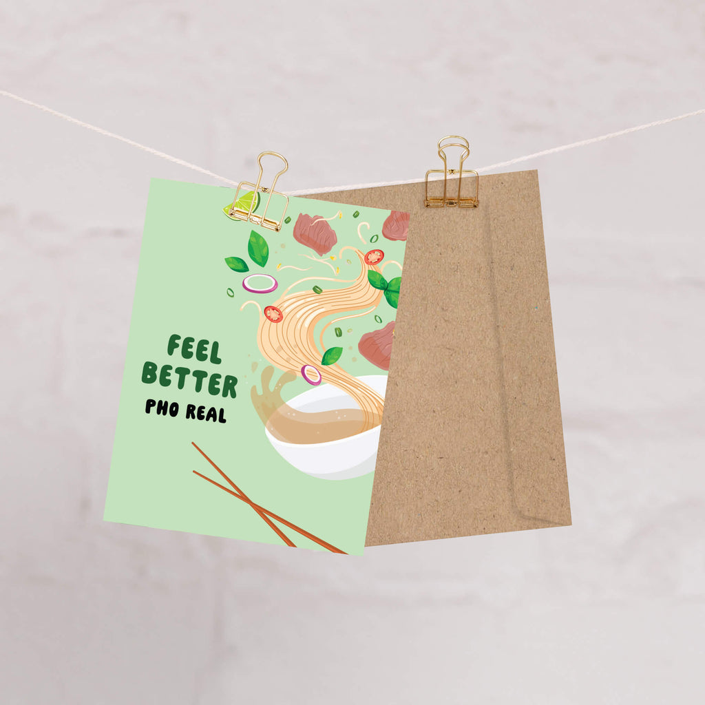 Card with 'Feel Better Pho Real' text and a bowl of pho illustration on a string with a brown envelope.