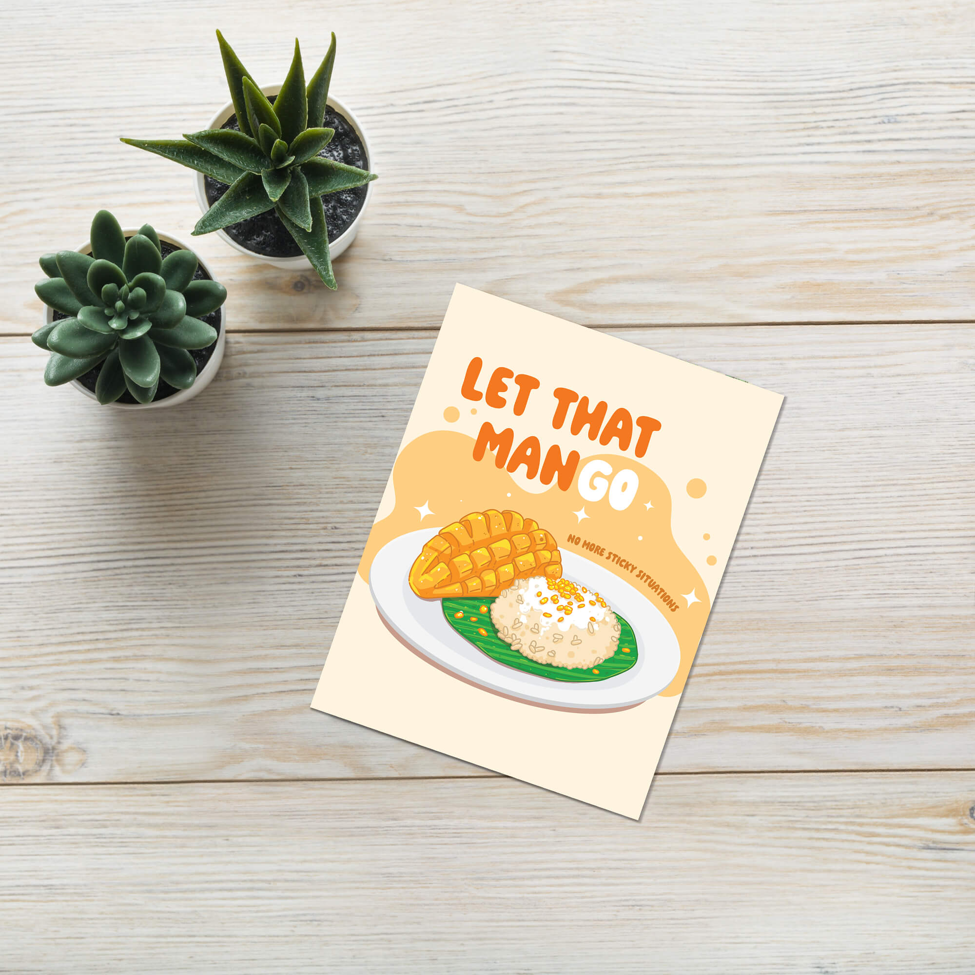 Card with mango and rice illustration and 'Let that mango' text on a wooden surface with plants.