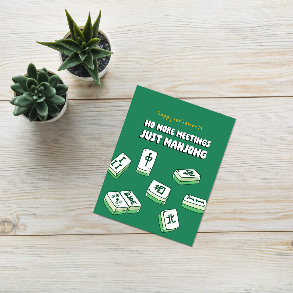 Green card with Mahjong tiles and text on a wooden surface with plants
