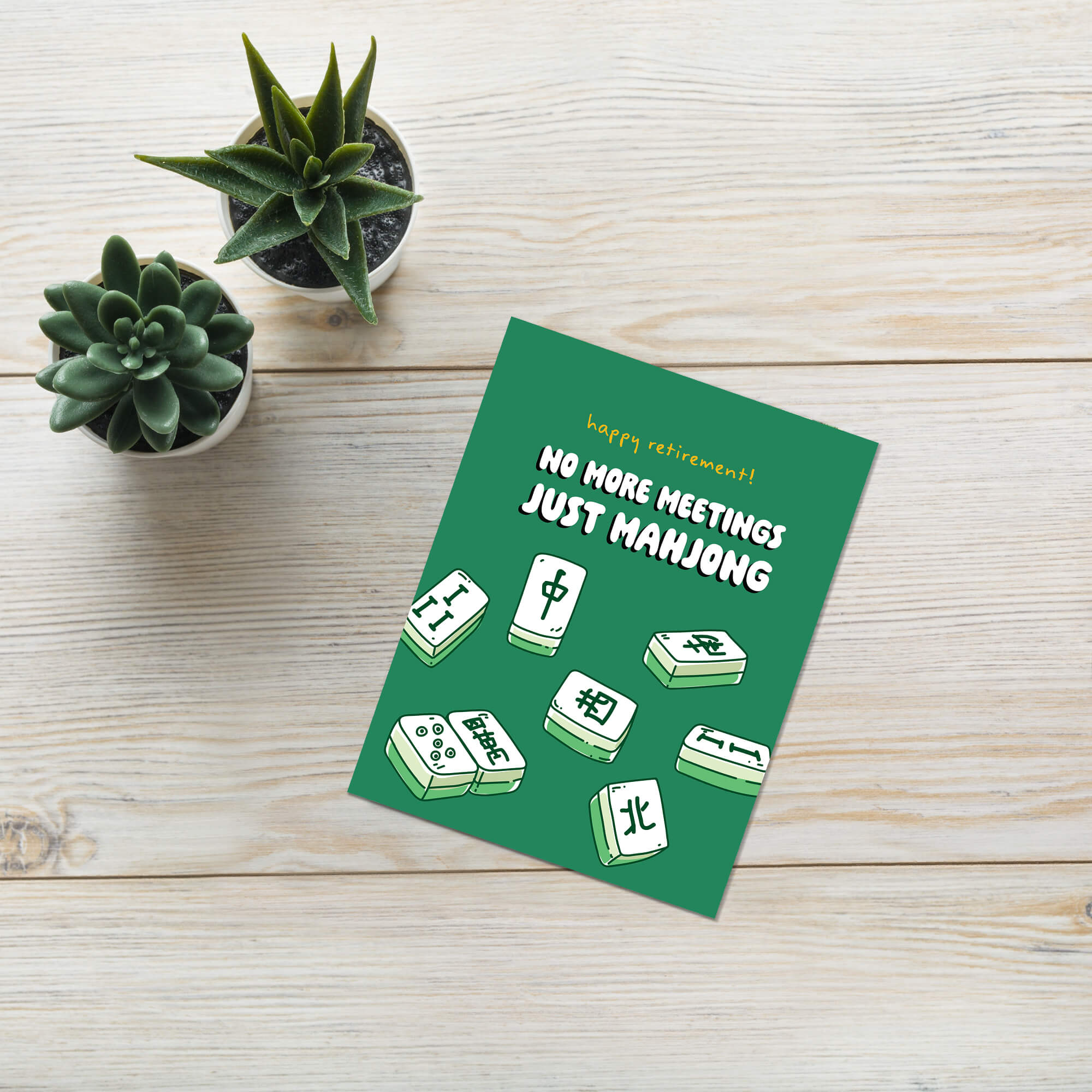 Green card with Mahjong tiles and text on a wooden surface with plants