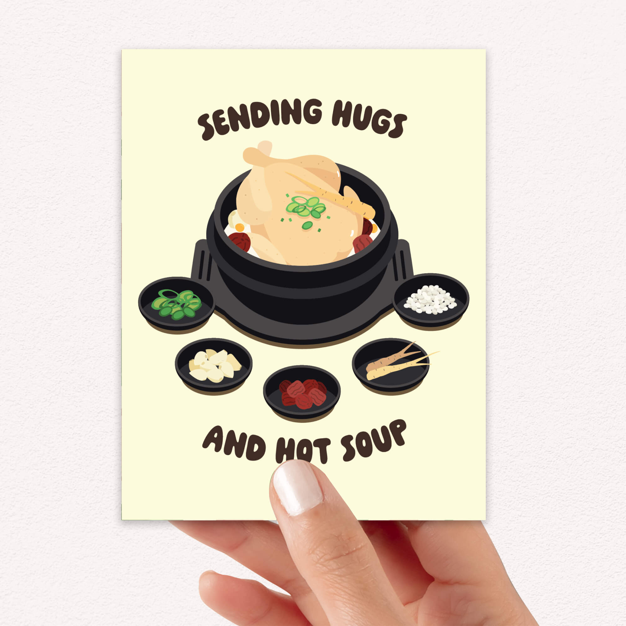 asian Greeting card with a cartoon illustration of a korean chicken soup and text 'Sending Hugs and Hot Soup' on a beige background.