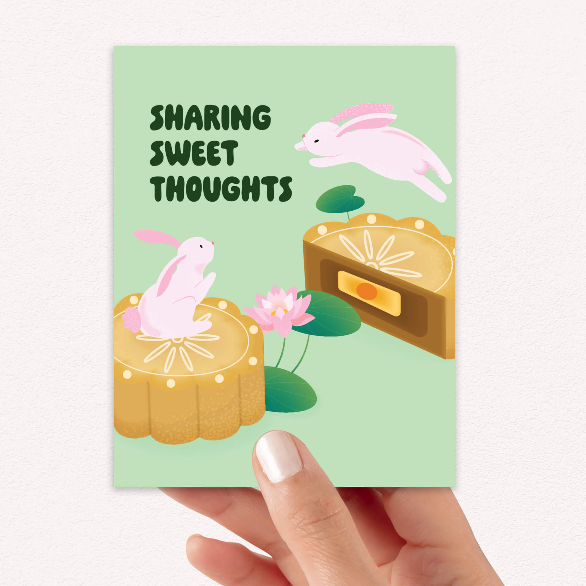 Card with rabbits and mooncakes on a light green background, held by a hand.