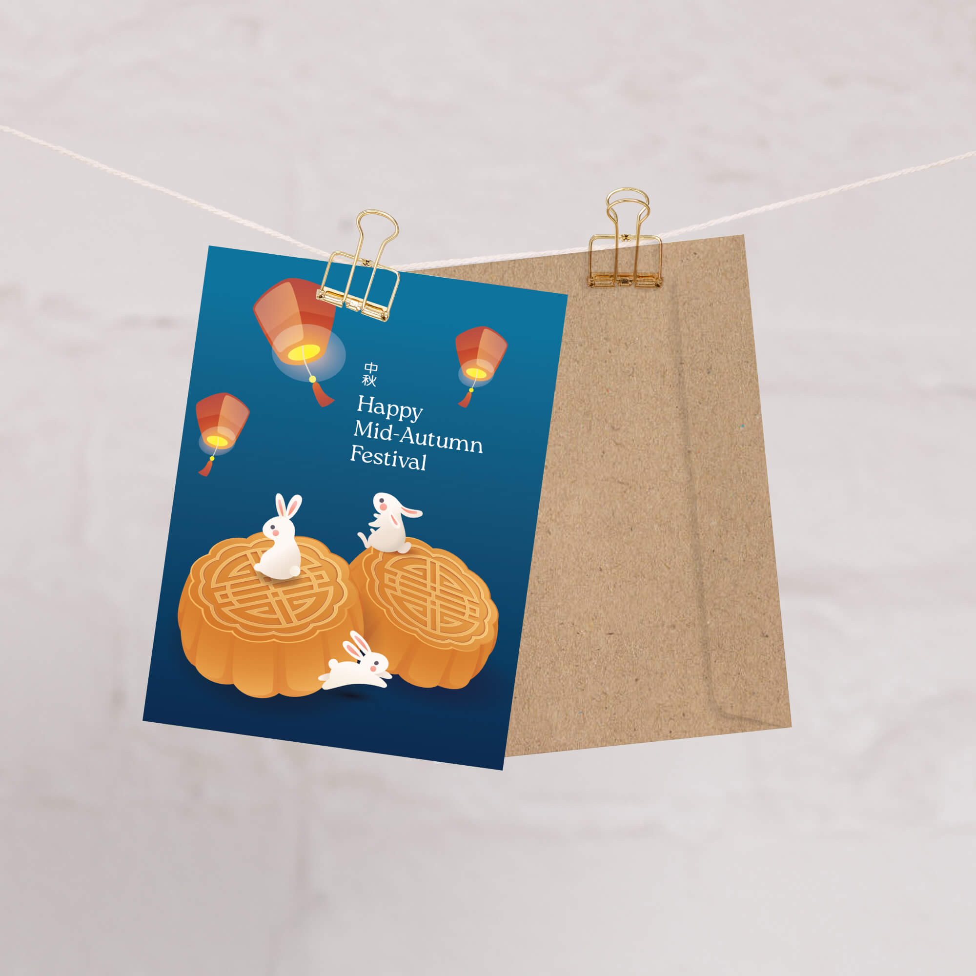 chinese greeting Card with rabbits on pumpkins and lanterns, text 'Happy Mid-Autumn Festival', attached to a string with a gold clip.