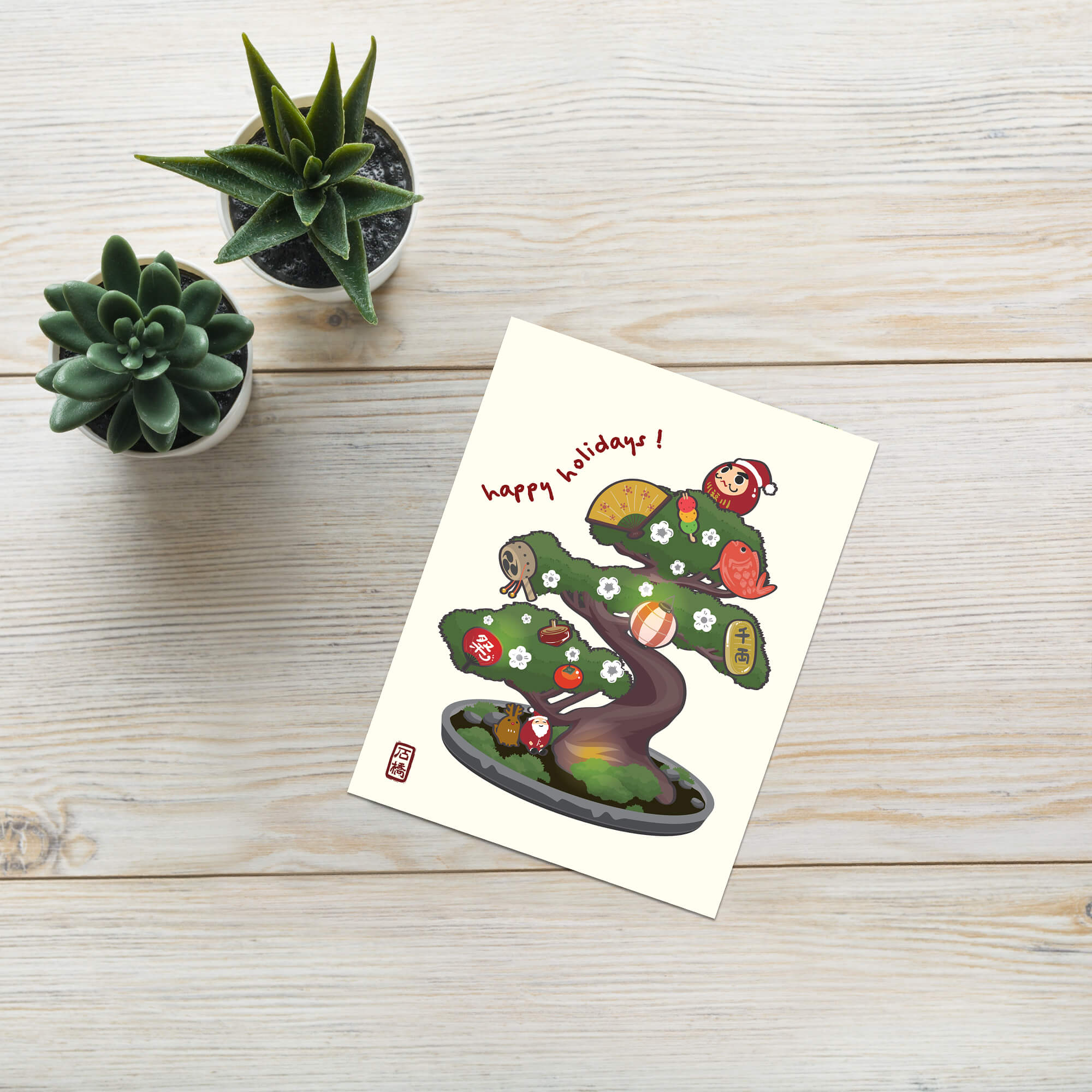 cute japanese christmas card with an Illustration of a bonsai tree decorated with lucky charms, daruma, and red lanterns. Text reads “happy holidays!”