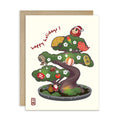 cute japanese christmas card with an Illustration of a bonsai tree decorated with lucky charms, daruma, and red lanterns. Text reads “happy holidays!”
