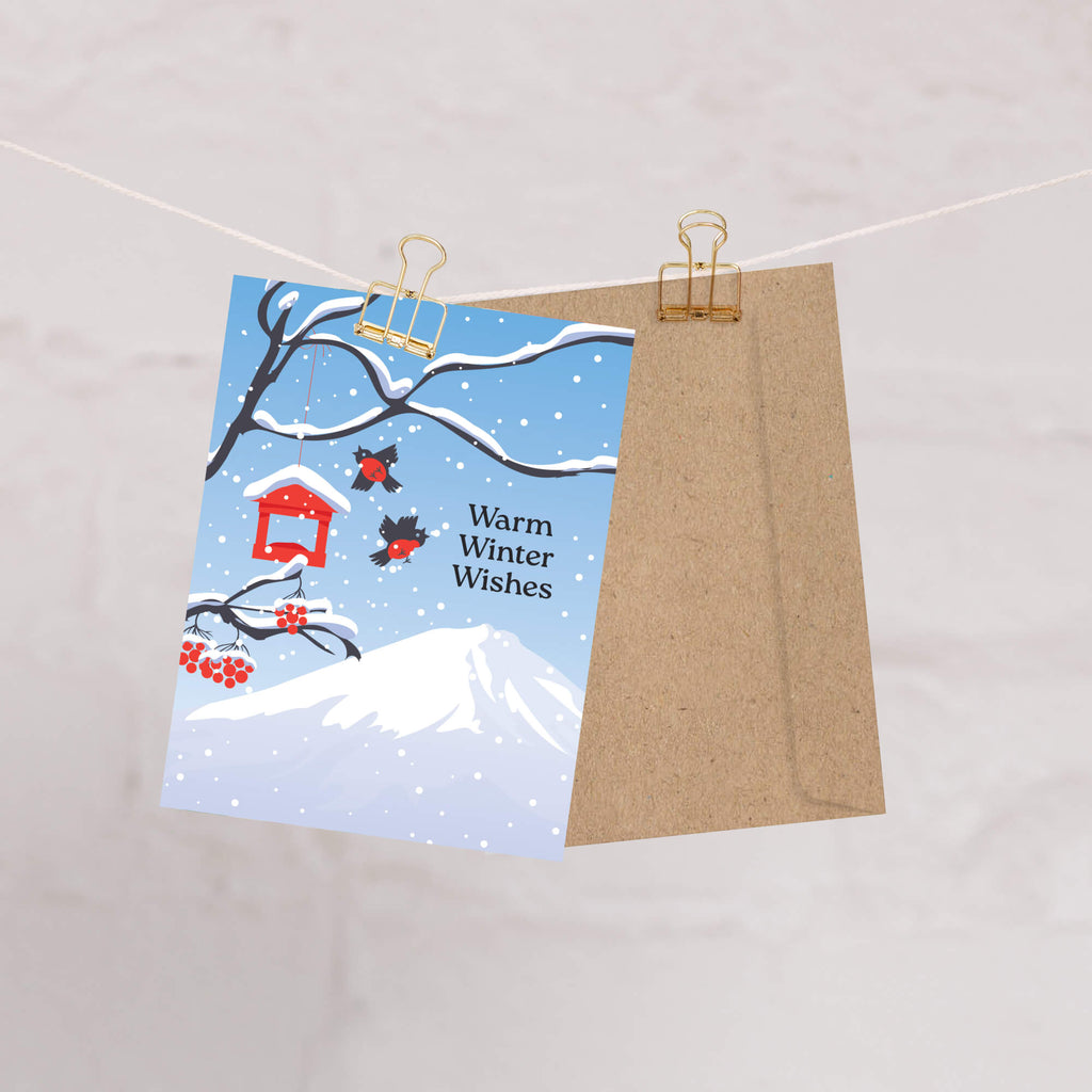unique japanese christmas card. Snow-covered tree branches with red berries, birds, a red birdhouse, and Mt. Fuji. Text reads “Warm Winter Wishes.”