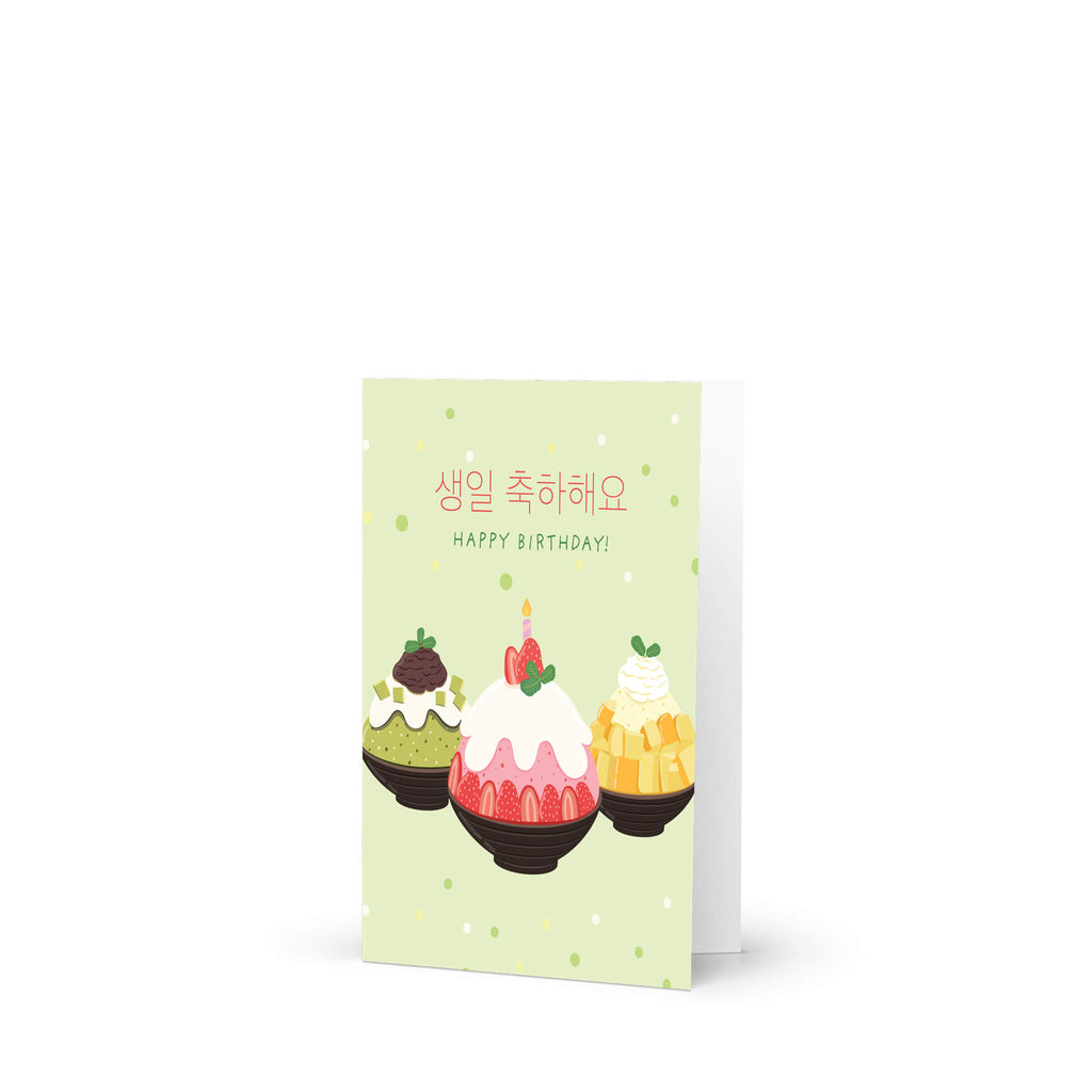 A Korean birthday card with a light green background, featuring three illustrated desserts and the text '대댄대 대날대북도!' and 'HAPPY BIRTHDAY!' in Korean and English. The card is shown standing upright against a clean white background.