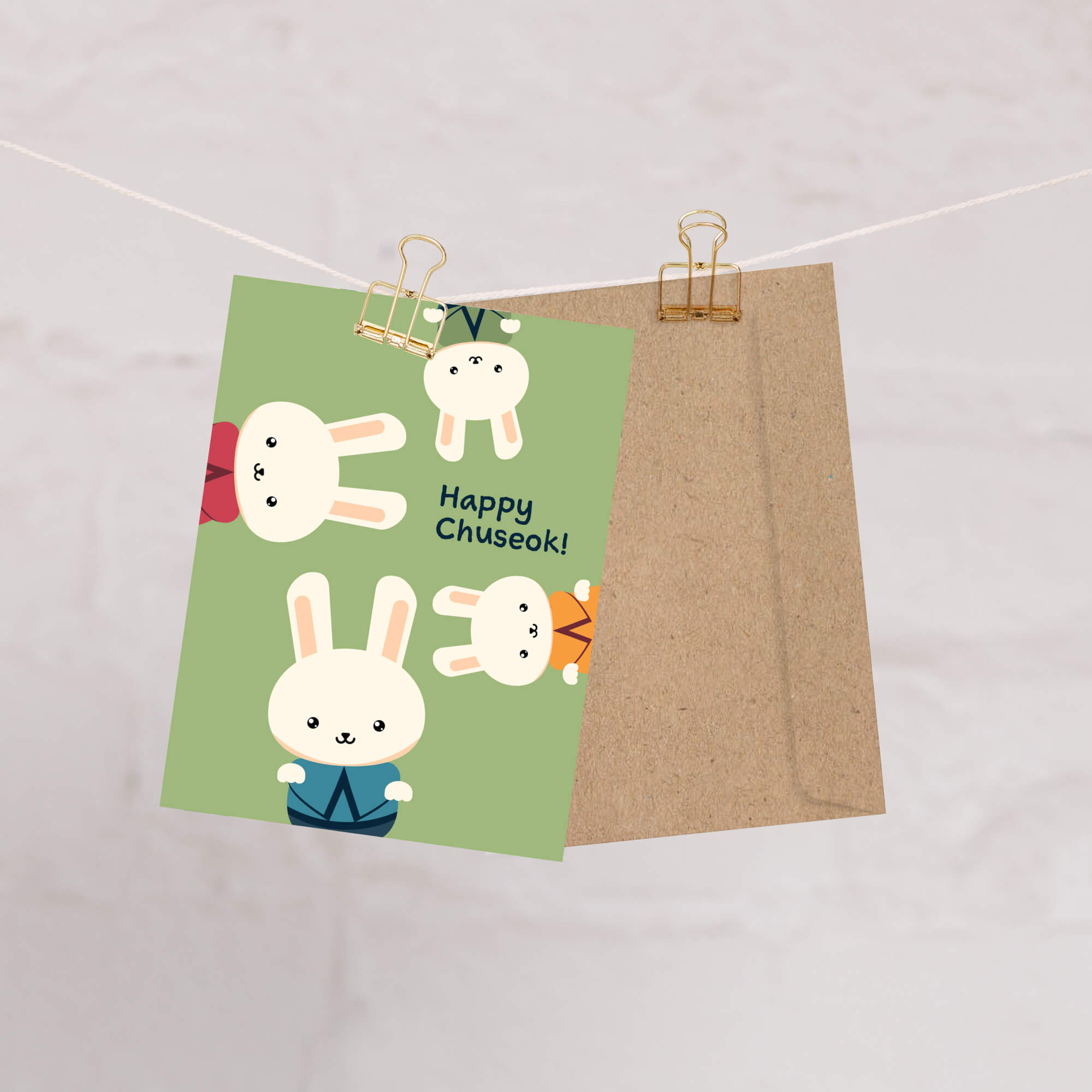 korean harvest thanksgiving greeting Card with cartoon bunnies and 'Happy Chuseok!' text on a green background, attached to a brown envelope with gold clips.