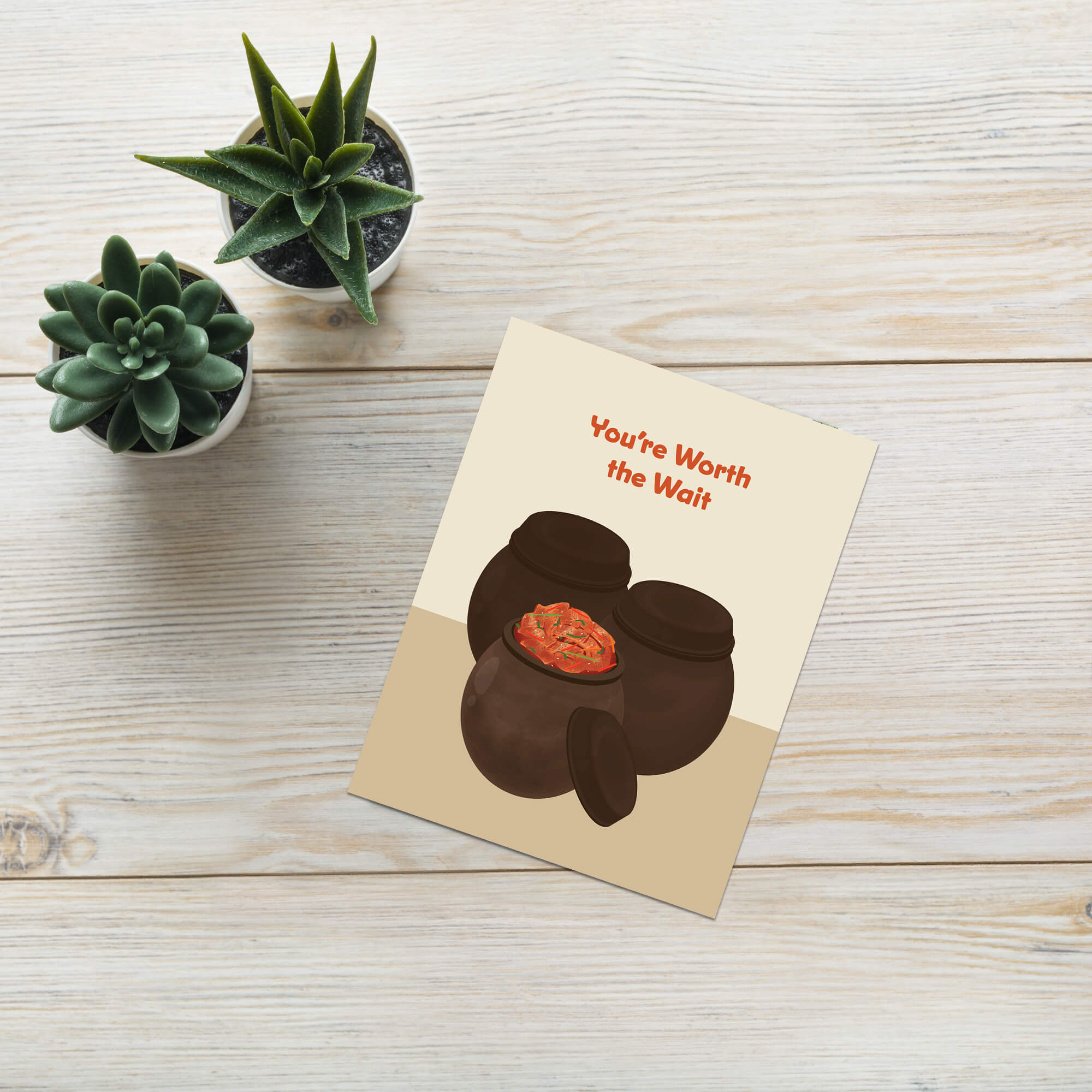 Greeting card with two traditional korean fermenting pots and a kimchi cabbage inside, text 'You're Worth the Wait' on a beige background.