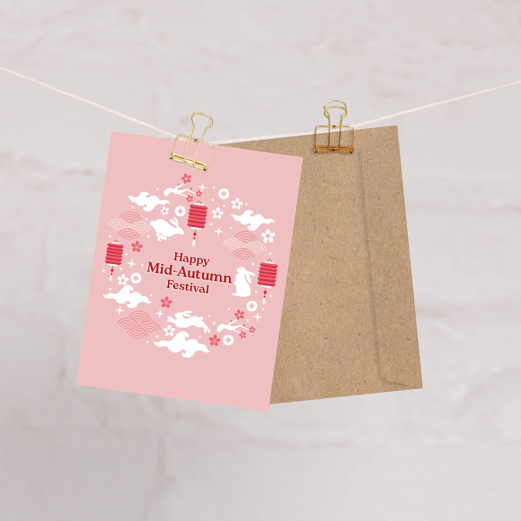 Pink card with white graphics and text on a string, with a brown envelope underneath.