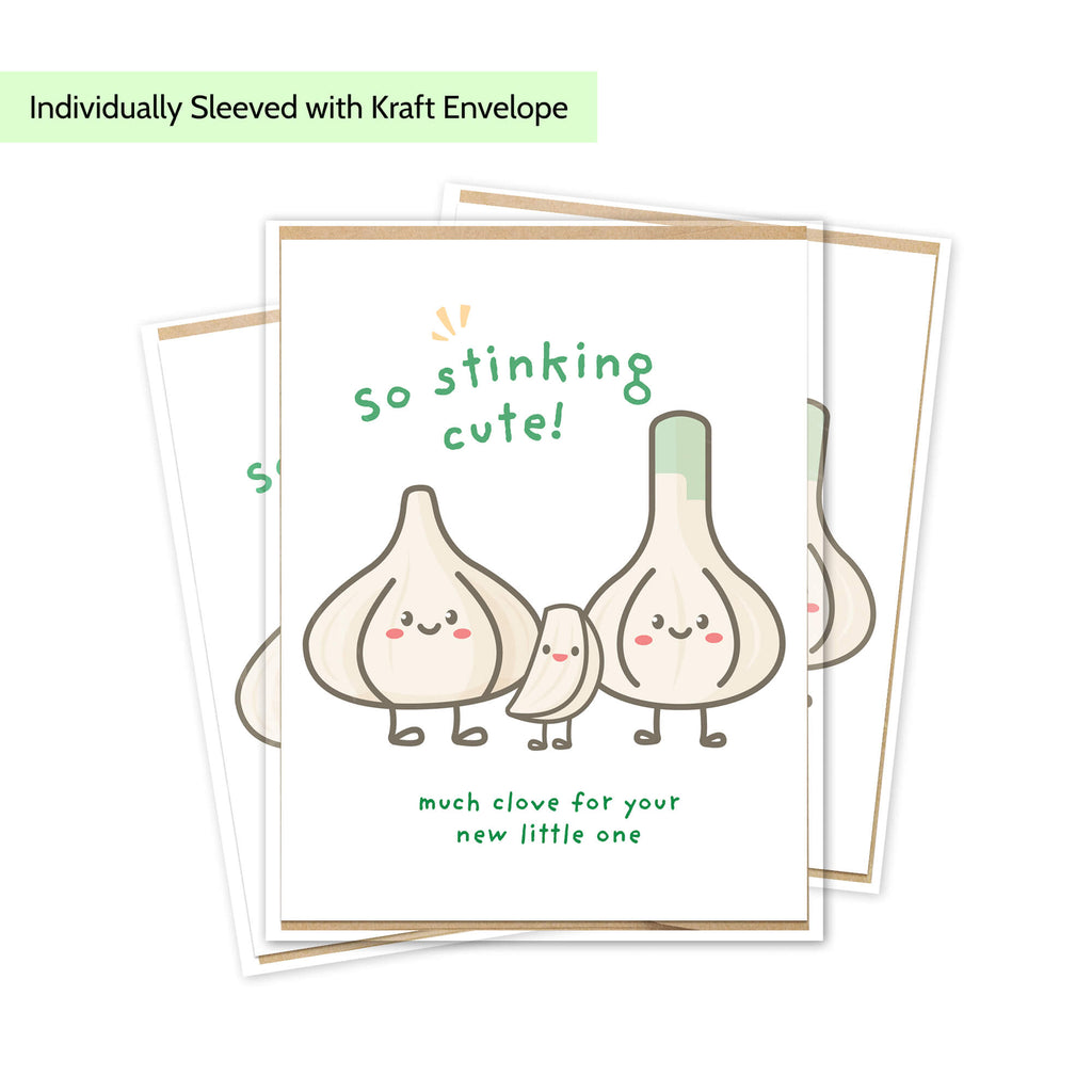 A funny baby shower card with a cute garlic illustration and the text 'so stinking cute!' and 'much clove for your new little one,' shown with kraft envelopes behind it on a white background. A light green label at the top reads 'Individually Sleeved with Kraft Envelope.