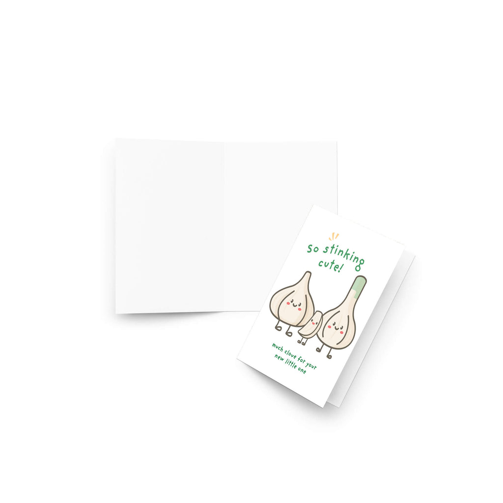 A funny baby shower card with a cute illustration of two garlic bulbs and the text 'so stinking cute!' and 'much love for you my love you not', shown with an open white envelope on a white background.