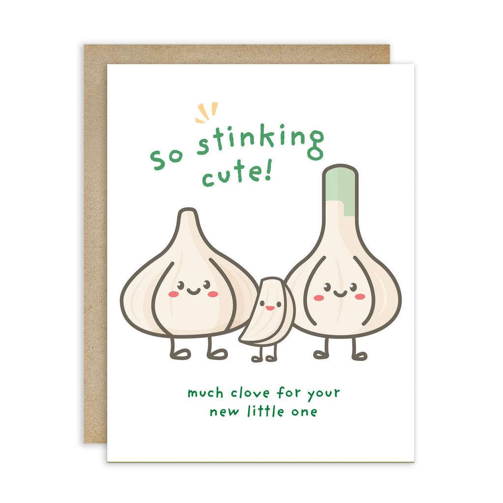A funny baby shower card with a brown kraft envelope behind it, featuring a cute illustration of three garlic bulbs with faces and the text 'so stinking cute! much clove for your new little one'.