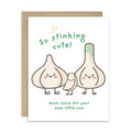 A funny baby shower card with a brown kraft envelope behind it, featuring a cute illustration of three garlic bulbs with faces and the text 'so stinking cute! much clove for your new little one'.