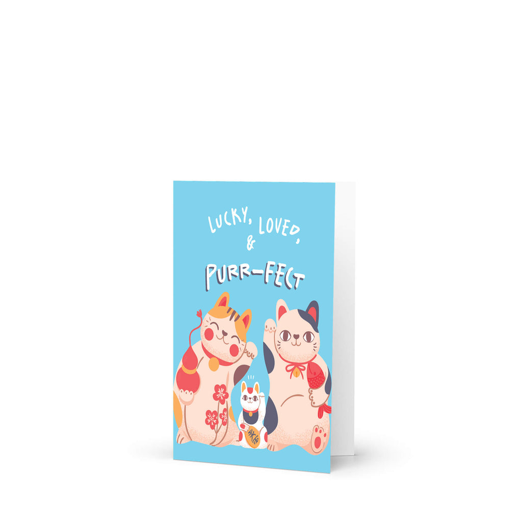A new baby greeting card with a light blue front cover featuring three cute illustrated cats and the text 'LUCKY, LOVED, PURR-FECT'. The card is shown standing upright against a clean white background.