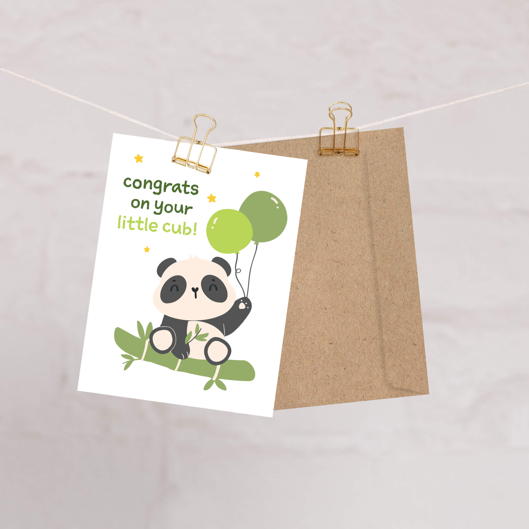 A new baby shower card featuring a cute cartoon panda holding green balloons, clipped to a string next to a brown kraft envelope on a light marble-like background.