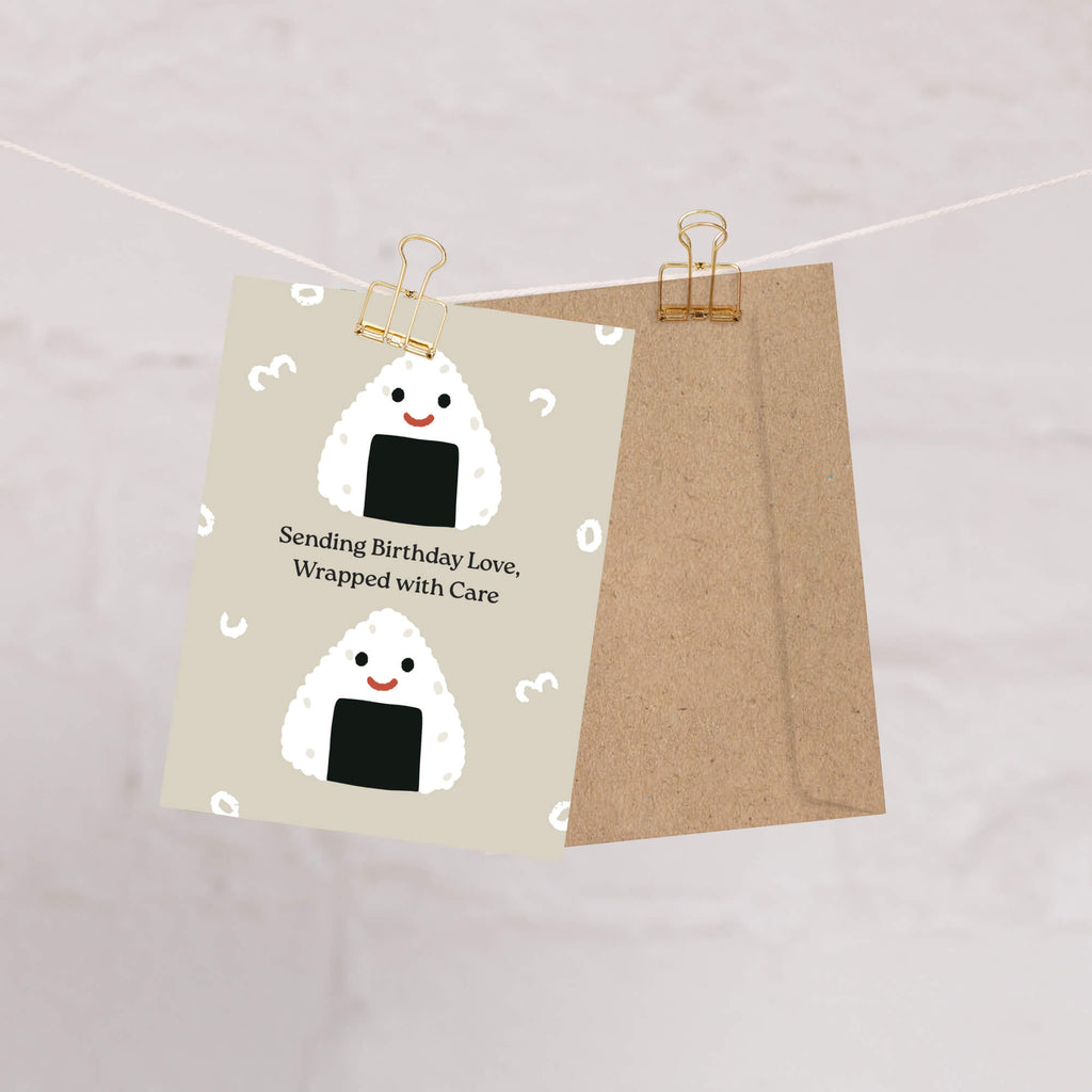 Card with cartoon rice balls and birthday message on a string with paper clips.