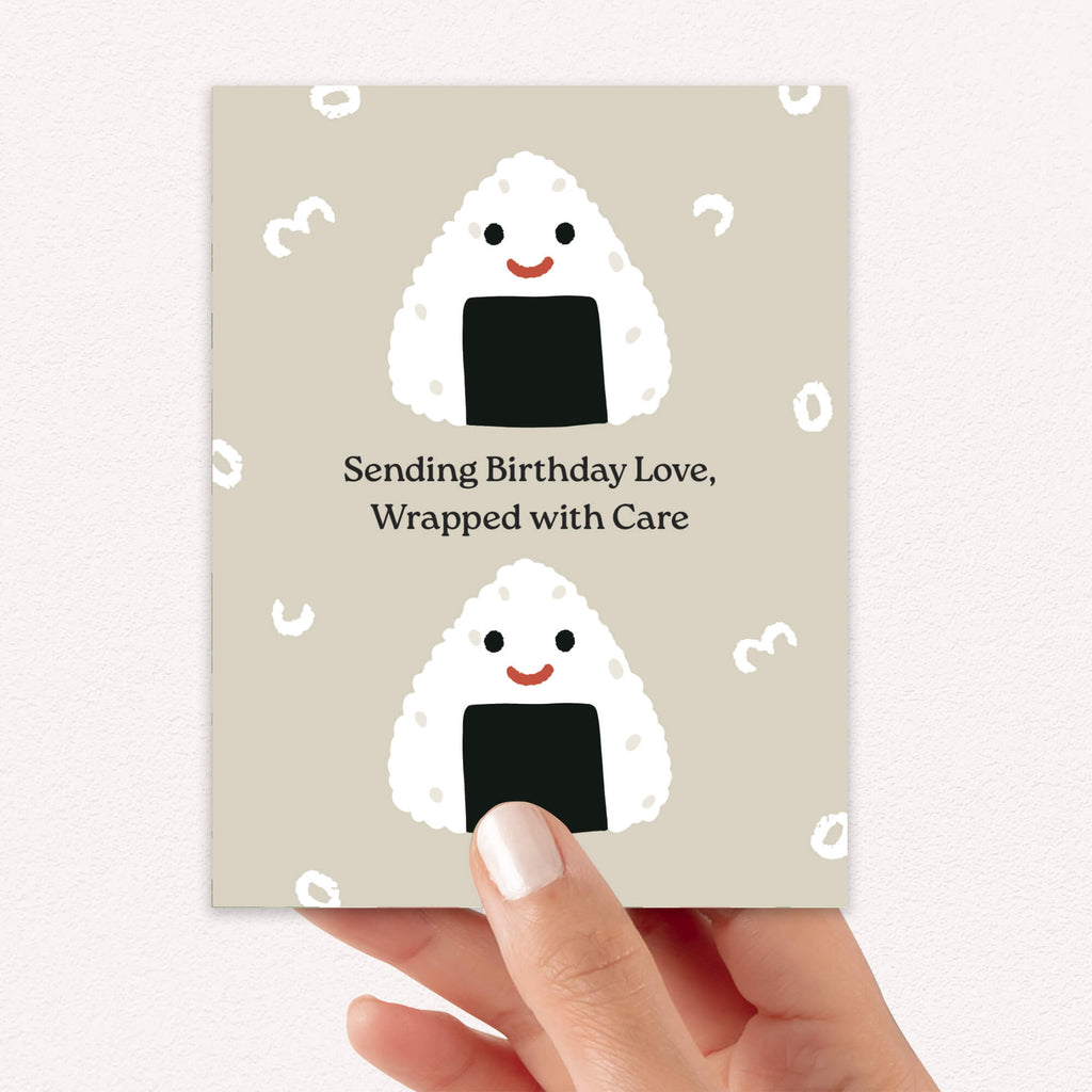Greeting card with cartoon rice balls and birthday message, held by a hand.