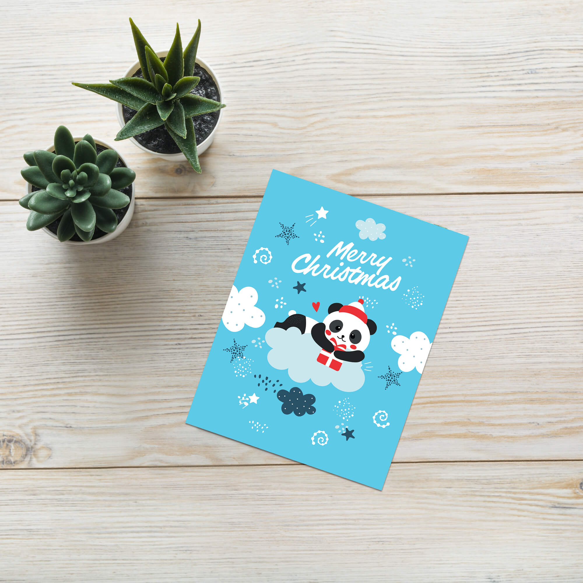 cute christmas card with A panda wearing a Santa hat floats on a cloud holding a red gift box. Surrounded by stars and snowflakes. Text reads “Merry Christmas.”