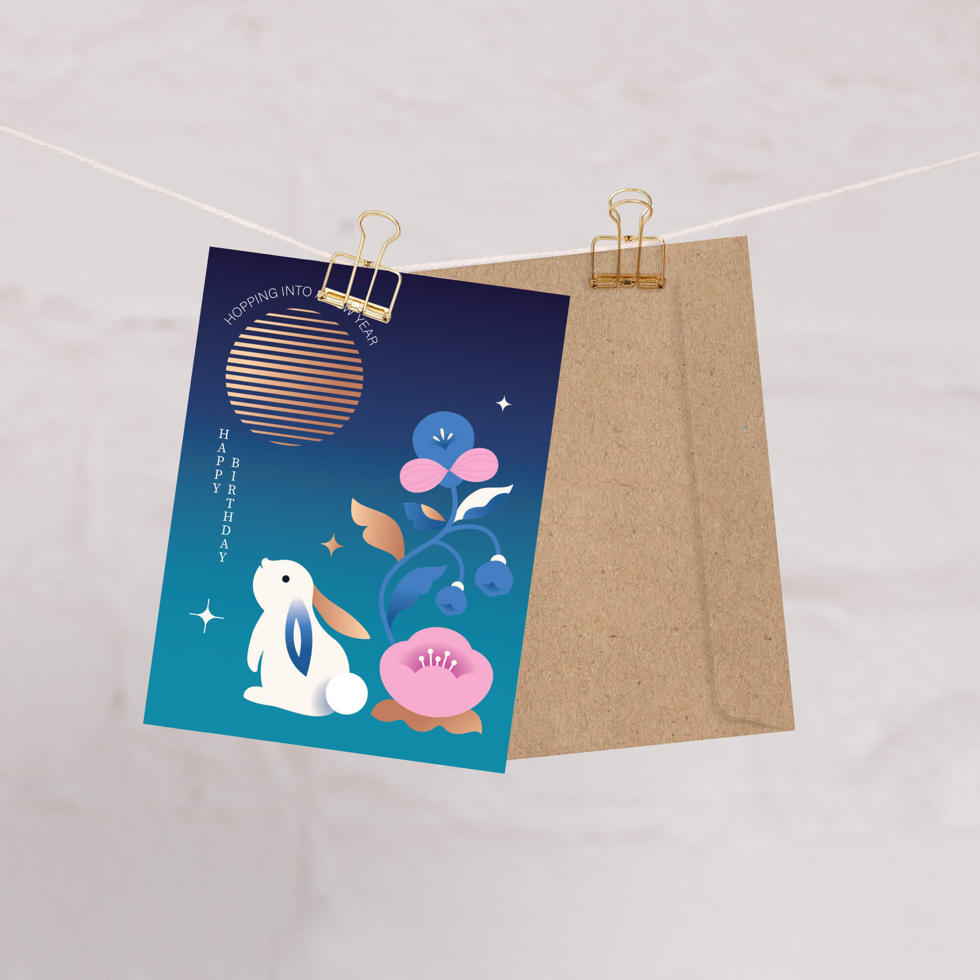 birthday Greeting card with a rabbit and flowers design on a blue background, clipped to a string with a brown envelope.