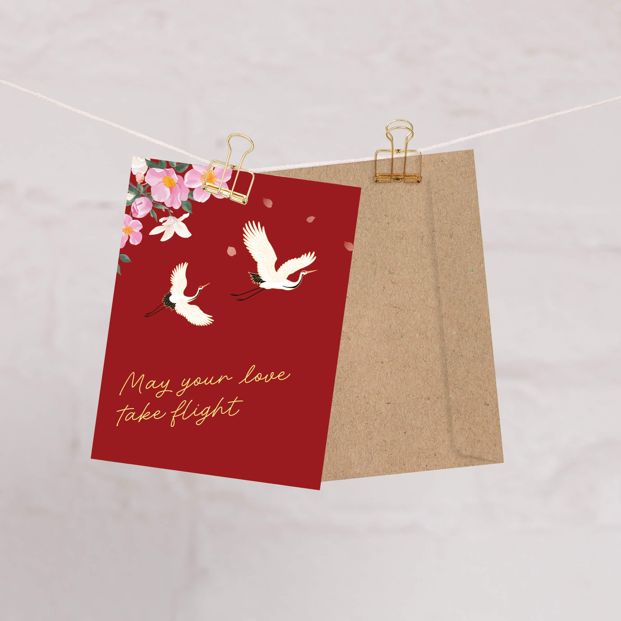 Red wedding greeting card with white birds and flowers with text: may your love take flight, and a brown envelope on a light gray background.