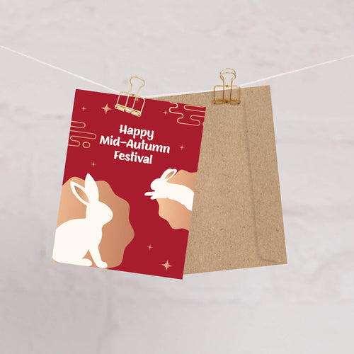 chinese inspired greeting Card with rabbits and 'Happy Mid-Autumn Festival' text on a red background, attached to a string with a clip.