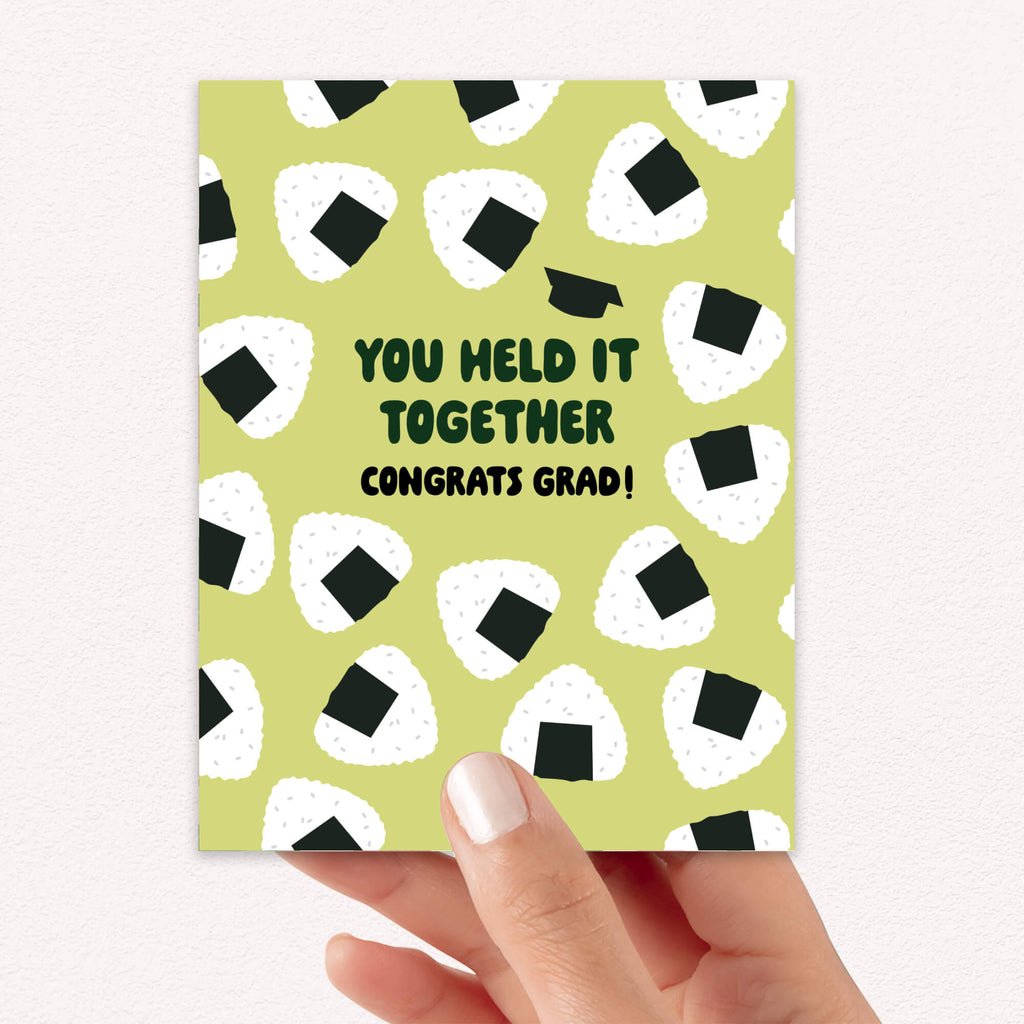 Graduation card with japanese onigiri rice ball pattern and text 'You held it together. Congrats grad!' on a white background.